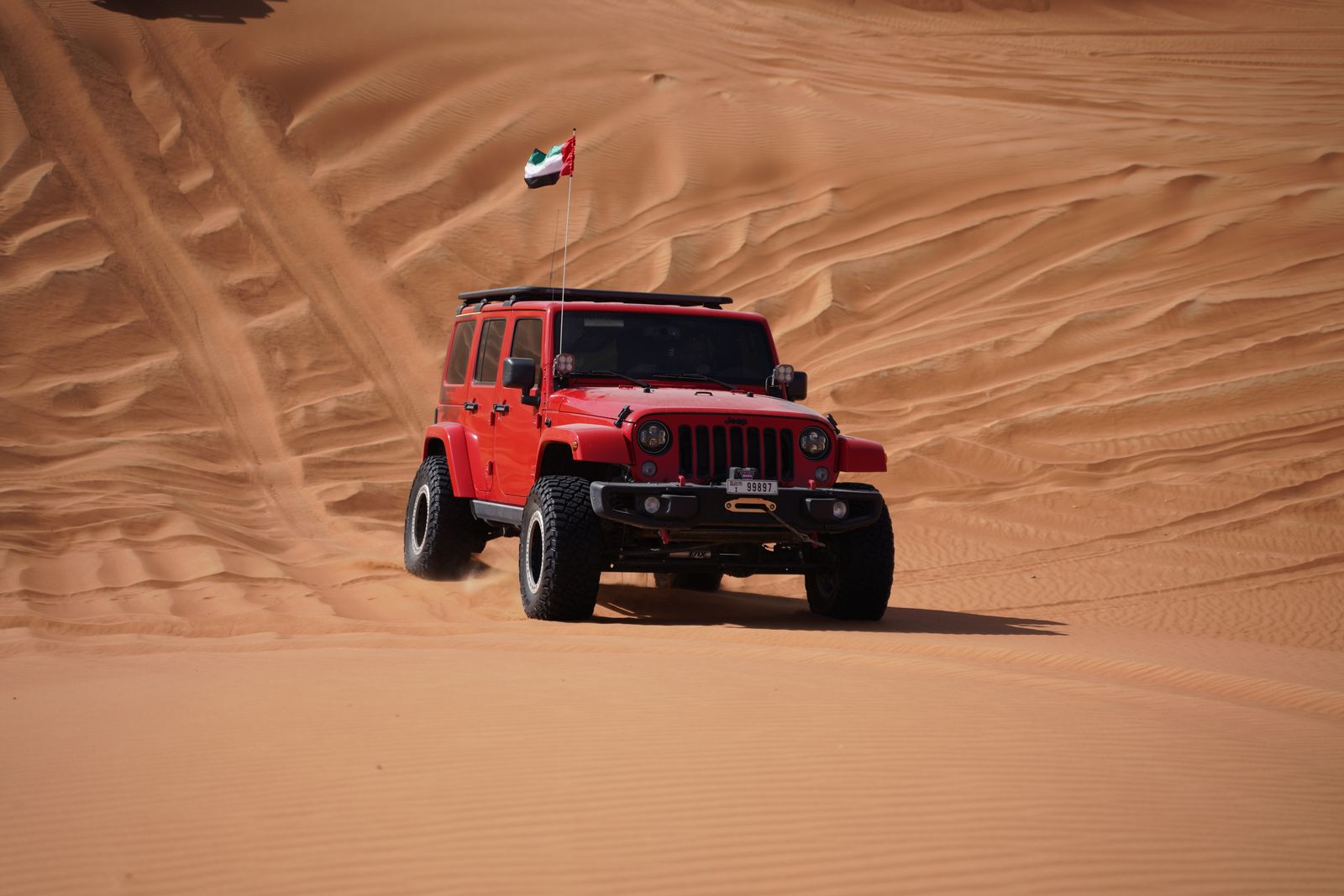 A red SUV with a flag drives through desert sand dunes, capturing the essence of off-road adventure.